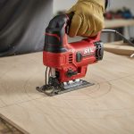 Woodworker guiding compact jigsaw along marked curved line on plywood for precise cut