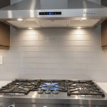 Stainless steel range hood mounted above gas cooktop showing proper sizing with three inches extending beyond burners on each side
