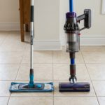 A microfiber mop and cordless vacuum placed side by side on a clean ceramic tile floor