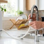 Person connecting a portable countertop dishwasher hose to a kitchen sink faucet.